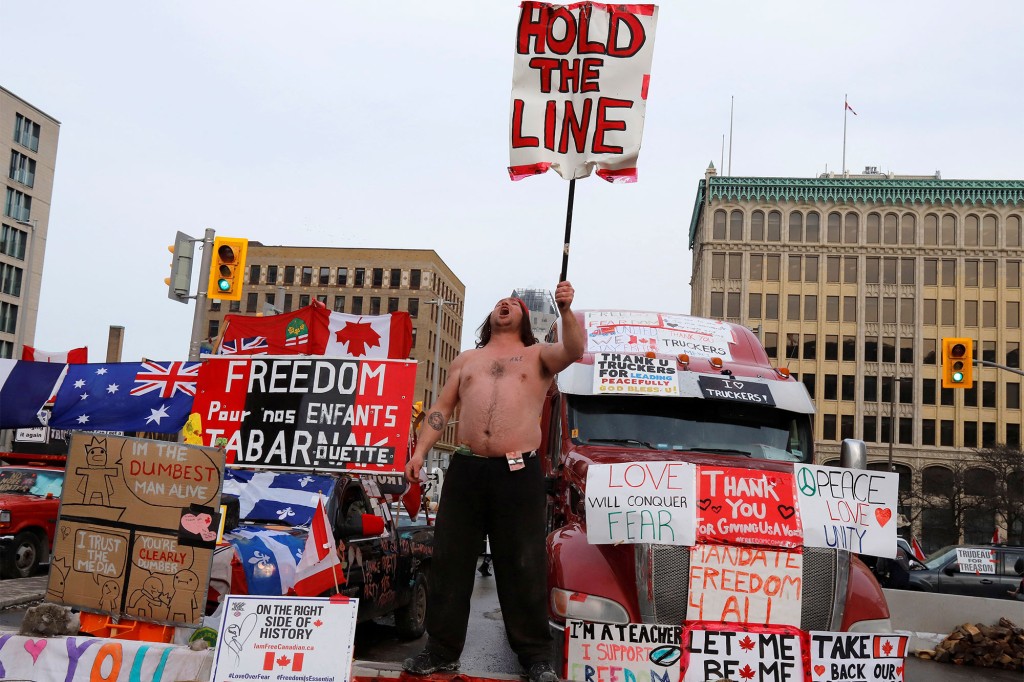 Osoba trzyma znak przed ciężarówkami blokującymi ulicę w centrum miasta, podczas gdy kierowcy ciężarówek i ich zwolennicy nadal protestują przeciwko nakazom szczepionki na koronawirusa (COVID-19) w Ottawie, Ontario, Kanada.