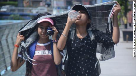 Dwie młode dziewczyny zakrywają głowy, spacerując i pijąc wodę w upalnym popołudniowym upale w Bombaju w Indiach.