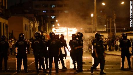 Policjanci w Limie stoją przed płonącym budynkiem handlarza podczas demonstracji przeciwko peruwiańskiemu prezydentowi Pedro Castillo.  Rozpoczęły się protesty przeciwko podwyżkom cen paliw i nawozów wywołane konfliktem na Ukrainie, ale ich zakres się poszerzył.