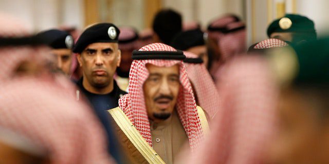 PLIK – 24 stycznia 2015 r. archiwalne zdjęcie saudyjskiego króla Salmana strzeżonego przez jego ochroniarza generała dywizji Abdulaziz Al-Fagham, w tle, gdy uczestniczy w przyjęciu w Pałacu Królewskim Diwan w Rijadzie w Arabii Saudyjskiej.  (AP Photo/Yoan Valat, Pool, File)